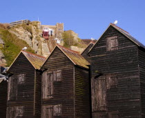 Black wooden huts used for storing fishing nets.The East Hill Lift funicular railway behind.