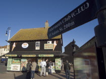 Customers queuing at a seaside take away. A sign with directions to the Fisherman s club in the foreground