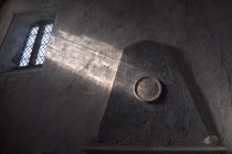 Boxgrove Priory Church of St Mary and St Blaise. Interior view of  light shining through small window onto a wall and marble monument.