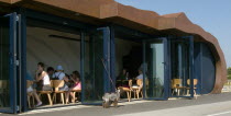 Customers sitting at tables inside the East Beach Cafe designed by Thomas Heatherwick. Dog tied to glass door waiting outside