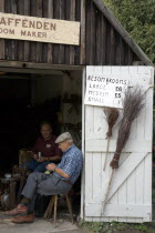 Amberley Working Museum. The Broom maker workshop with two men sitting in doorway next to display of brooms