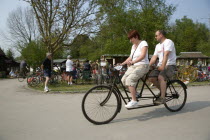 Amberley Working Museum. Veteran Cycle Day Grand Parade. Man and woman riding a riding a Tandem bicycle with visitors watching.