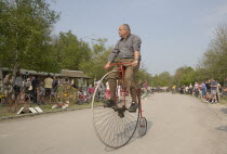 Amberley Working Museum. Veteran Cycle Day Grand Parade. Man wearing period custom riding a Penny Farthing bicycle with visitors watching.