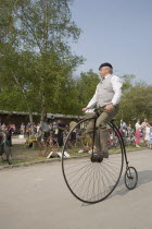 Amberley Working Museum. Veteran Cycle Day Grand Parade. Man wearing period custom riding a Penny Farthing bicycle with visitors watching.