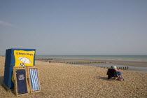 Deck chair hire station on sand and shingle beach with a woman sitting on a chair looking out towards the sea
