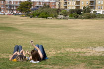 Two girls lying on grass by seafront promenade using and sharing an MP3 music player