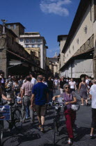 Ponte Vecchio Bridge. People walking along street lined with shops and stalls next to the bridge.