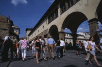 Ponte Vecchio Bridge with visitors walking along street lined with shops and stalls by the bridge arches