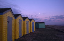 Row of  yellow and green beach huts next to promenade seen in evening light