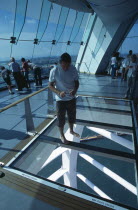 Gunwharf Quay, The Spinnaker Tower. Interior on the observation deck with a man standing on a glass floor viewing the harbour below.