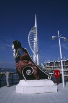Gunwharf Quay, The Spinnaker Tower with figurehead in the foreground and a man standing on waterfront promenade looking out across the harbour