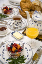 Breakfast table setting with fresh fruit in a bowl  orange juice in a glass  tea in a cup  a teapot  marmalade  butter in a bowl  croissant and toast