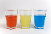 Soda glasses containing light red  yellow and blue coloured soft drinks