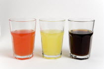 Soda glasses containing light red  yellow and dark coloured cola soft drinks