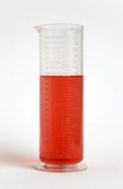 Plastic measuring beaker containing light red liquid and showing measurements in both millimeters and fluid ounces