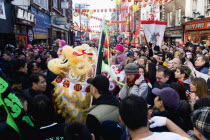 Crowds passing under paper lanterns hung around one of the oriental ornamental gates or paifang in Gerrard Street following an embroidered banner during Chinese New Year celebrations in 2006 for the coming Year of The Dog