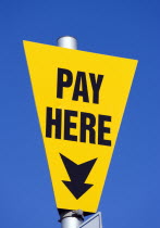 Yellow car park sign against a blue sky with black writing saying Pay Here