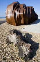 The rusted metal structure of the fish and seafood restaurant the East Beach Cafe designed by Thomas Heatherwick on the promenade with driftwood on the pebble beach in the foreground