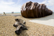 Two people standing on the beach looking at the rusted metal structure of the fish and seafood restaurant the East Beach Cafe designed by Thomas Heatherwick with an A-frame on the promenade and driftw...