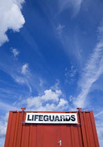 Red shipping container used as a lifeguards hut on the beach with expansive blue sky overhead