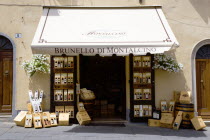 ITALY, Tuscany, Montalcino, Val D'Orcia Brunello di Montalcino wine shop or enoteca in the medieval hilltown with a display of wines on the pavement beside the doorway under a canopy.