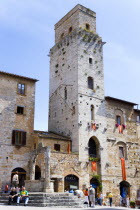 ITALY, Tuscany, San Gimignano, People gathering around the well in the Piazza della Cisterna with one of the town's medieval towers beyond above shops.