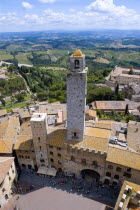 ITALY, Tuscany, San Gimignano, People in the Piazza del Duomo with the medieval town's oldest tower of the Palazzo Vecchio Podesta built in 1239 with the farmland east of the town beyond.
