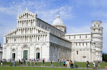 ITALY, Tuscany, Pisa, The Campo dei Miracoli Field of Miracles. Tourists walking past the 12th Century Lombard-style facade of the Cathedral or Duomo with the 14th Century Leaning Tower beyond.