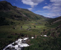 View west over Nant Ffrancon Valley from Ogwen Falls.  River winding across valley floor with small cultivated fields and pasture between steep  eroded hillsides.