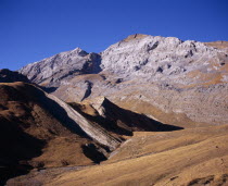 Sierra de Tendenera and highest point Pico de Tendener.  Peaks from left to right  2823 - 2853 m.  Grey  eroded rock and scree with golden brown grass covering lower slopes