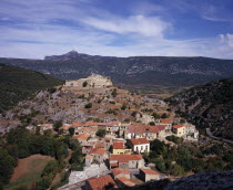 Fenouillet.  View from Chateau Sabarda over streets and red tiled rooftops of village houses with ruins of Chateau St Pierre on hillside above.