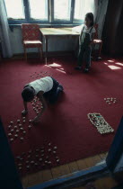 Children playing indoors with sheep knuckle bones used to represent herds and pens.