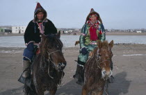 Buriyat ethnic minority couple in traditional dress riding horses with frosted coats and whiskers.