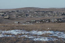 View towards typical small town in open landscape with patches of melting snow in the foreground.
