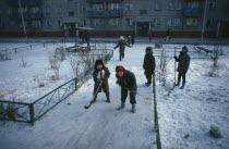 Children playing ice hockey along pavements in winter snow.