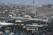 View over crowded Sunday market with houses stretched across hillside above and line of pylons.