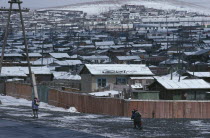 Snow covered rooftops of housing in city suburbs in winter with children wrapped up in warm clothing walking along road in foreground.