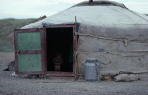 Young child standing inside open doorway of yurt wearing just a jumper and no trousers.