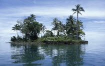 Malaita Province  Lau Lagoon.  Rocky  man made.  islet with palm trees and vegetation reflected in rippled water in foreground.