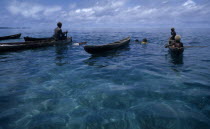 Malaita Province  Lau Lagoon. Spear fishing from wooden dug out canoes.  Dark turquoise sea with light reflections and blue sky.
