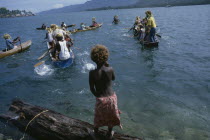 Malaita Province  Lau Lagoon.  Child watching wedding party depart by canoe.  Note rafia head dresses of rowers.