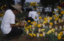 Tarascan Indian lighting candles on grave decorated with marigold flowers for Night of the Dead in Tzintzuntzan Cemetery.