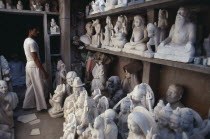 Marble carver in workshop with shelves of statues.