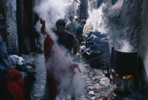 Street in the wool dyeing souk with man in foreground lifting skein of steaming yarn from vat of dye.