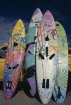 Colourful Windsurfing boards standing up against a truck on sandy beach