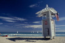 Lifeguard Tower displaying American flag with sailboats seen on turquoise sea behind