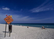 Road Construction Ahead sign on sandy beach with sunbathers