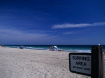 Designated Surfing Area Sign on sandy beach with sunbathers near the waters edge