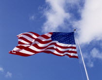 American Stars and Stripes National Flag blowing in the wind against a blue sky with clouds