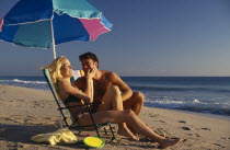 Young couple on sandy beach sitting under a parasol